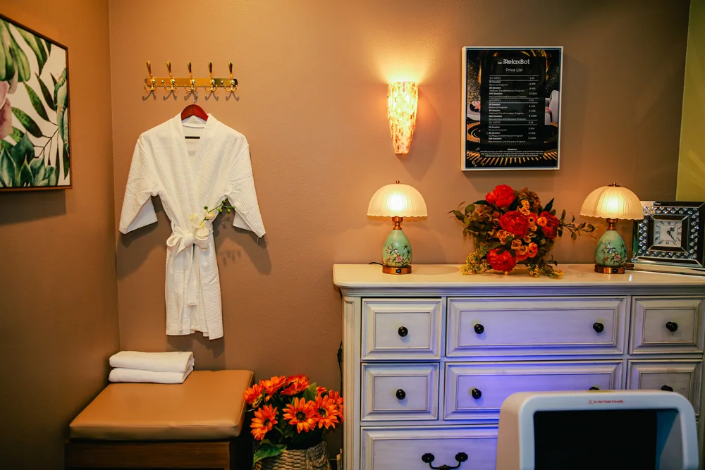 a spa robe hanging on brass hooks beside floral lamps and folded towels
