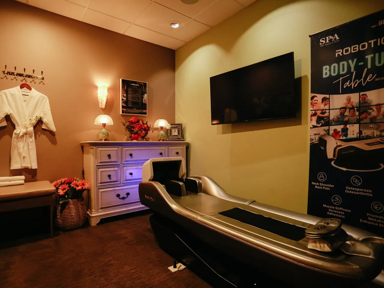 the iRelaxbot robotic massage bed — a silver Body-Tune table — in a private room, beside a wall screen and a benefits banner